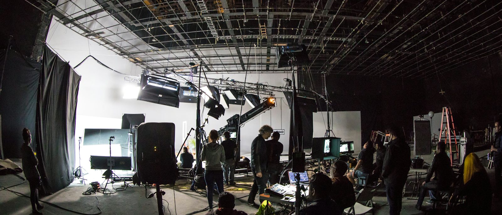 A large film crew at work under the lighting grid of a sound stage